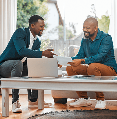 Two men sat down on a couch looking through documents together.