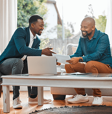 Two men sat down on a couch looking through documents together.