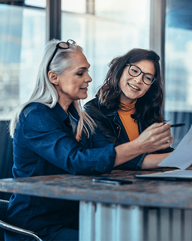 Two women sat down discussing whilst referring to a document.