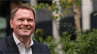 A close up shot of Scott Clay in front of a maintained garden.
