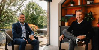 Two businessmen sitting casually in a beautiful office, smiling at the camera.