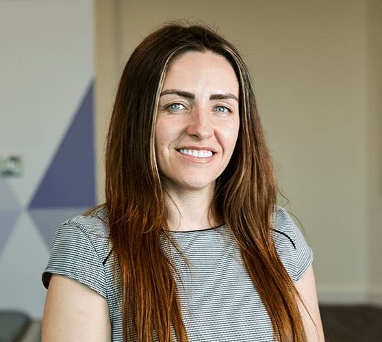 A woman with long brown hair smiling wearing a grey top.