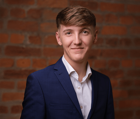 Freddie Atkinson with short light brown hair smiling in front of a red brick wall.
