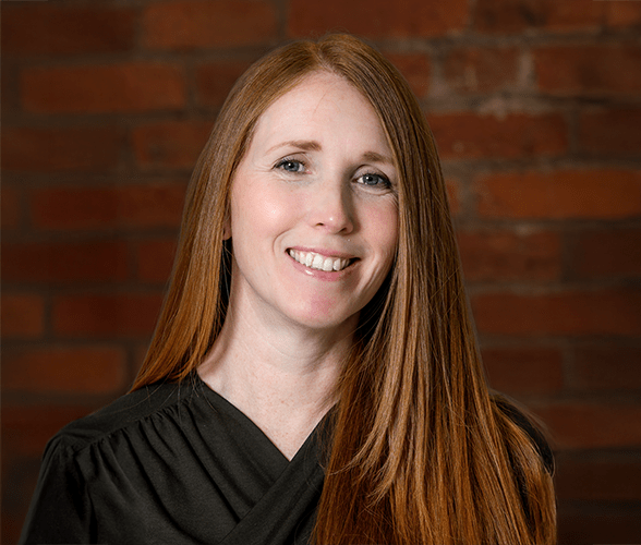 Sadie Harrison with long ginger hair smiling in front of a red brick wall.